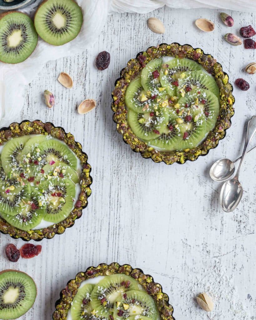 Véganes et sans cuisson, faites le plein de vitamines et d’énergie avec ces superbes tartelettes composées d’une pâte aux fruits secs (pistaches, cranberries, dattes), recouvertes de yaourt végétal et de tranches de kiwi bien fraîches !