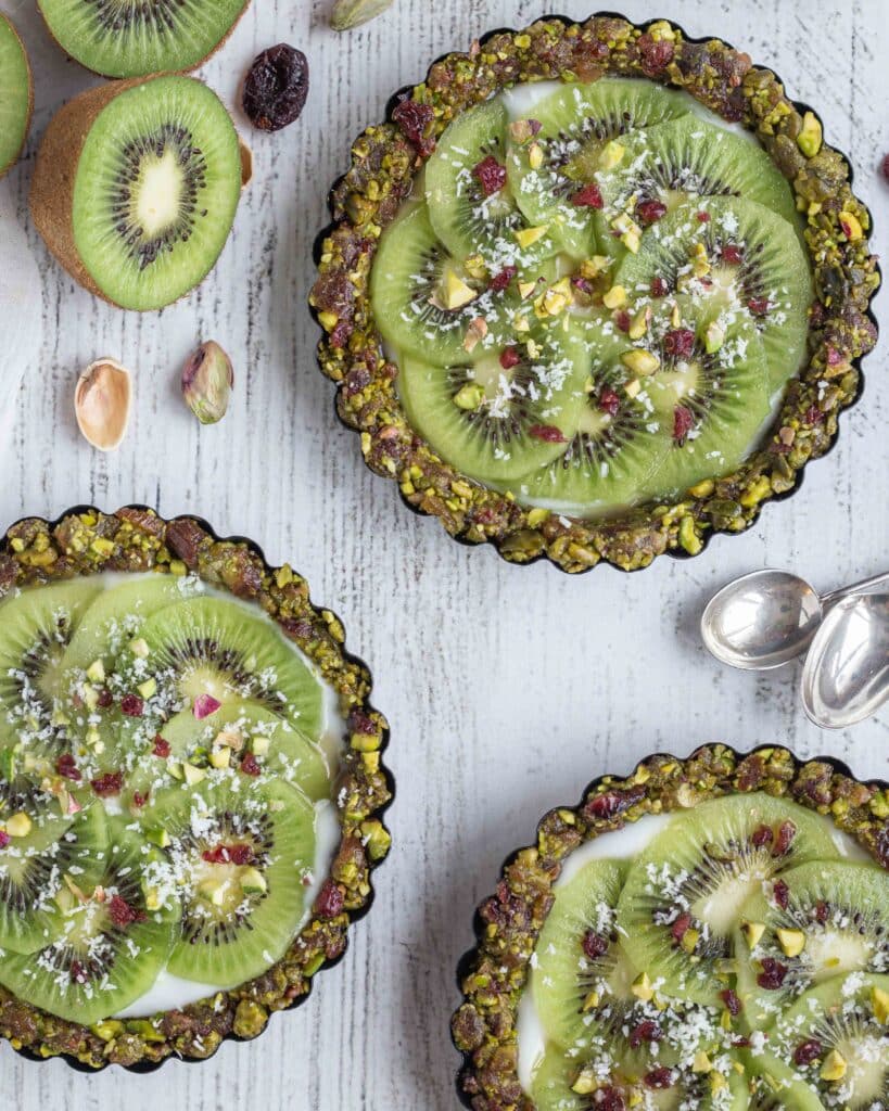Véganes et sans cuisson, faites le plein de vitamines et d’énergie avec ces superbes tartelettes composées d’une pâte aux fruits secs (pistaches, cranberries, dattes), recouvertes de yaourt végétal et de tranches de kiwi bien fraîches !