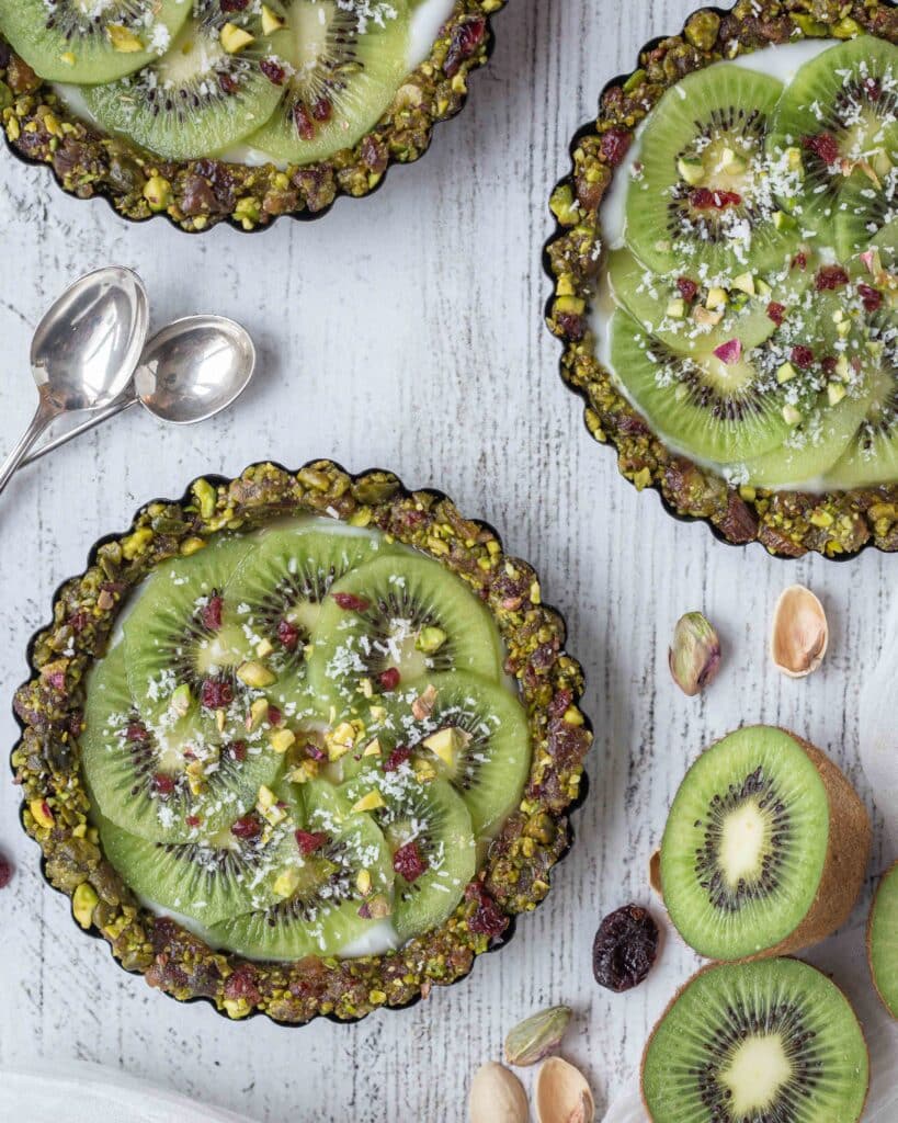 Véganes et sans cuisson, faites le plein de vitamines et d’énergie avec ces superbes tartelettes composées d’une pâte aux fruits secs (pistaches, cranberries, dattes), recouvertes de yaourt végétal et de tranches de kiwi bien fraîches !