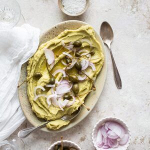 Fava grecque (purée de pois cassés) La Fava grecque est une purée de pois cassés. Normalement, elle se prépare avec des pois cassés jaunes. Mais, on n’en trouve pas facilement en France. Et comme mon père adore ça. Il a décidé de tester avec des pois cassés verts. Et le résultat est vraiment top ! Du coup, je vous donne sa recette ! C’est une recette à la fois simple et économique ! La liste des ingrédients est super courte et 100% vegan. Vous aurez simplement besoin de pois cassés, d’un peu d’huile, de thym. Un oignon jaune, un oignon rouge et des câprons. Ou à défaut de simple câpres ! La seule “difficulté” est qu’il faut anticiper un peu. En effet, comme pour toutes les légumineuses, les pois cassés ont besoin de tremper plusieurs heures. Avant de pouvoir être cuisinés. La petite astuce consiste à ajouter un peu de bicarbonate de soude dans l’eau de trempage. Cela permet de réduire un peu le temps de trempage. Notez qu’il faut toujours vider l’eau de trempage. Rincer les pois à l’eau claire. Et les faire cuire dans de l’eau “propre”. Une fois cuits, ils doivent simplement être mixés. Bien mixés. C’est bien meilleur si la consistance est bien lisse. Et voilà ! Quelques câpres et d’oignon rouge émincé. Et C’est fini ! C’est parfait à déguster comme du houmous. En apéro ou sur du pain, des pitas. Ou en accompagnement d’un plat grec ! Si vous aimez la nourriture grecque. Le blog regorge de recettes grecques ! Et je m’attèle à en ajouter toujours plus ! Vous pouvez notamment trouver les recettes familiales du tzatziki, de la feta au four. Ou même la recette de la spanakopita et des baklavas grecs ! Pour 2 personnes Temps de cuisson : 40min Temps de préparation : 25min Ingrédients 250g de pois cassés secs (verts ou jaunes) 1 càc de bicarbonate de soude 1 oignon jaune 2 càs d’huile d’olive 1 branche de thym 700ml d’eau Faire tremper les pois cassés dans un grand volume d’eau avec une càc de bicarbonate de soude pendant minimum 4h, idéalement toute une nuit. Jeter l’eau de trempage et rincer les pois. Hacher grossièrement l’oignon et le faire revenir dans une casserole avec l’huile d’olive et le thym pendant 3-4min. Ajouter les pois cassés et l’eau. Porter à ébullition, puis baisser le feu pour obtenir de petits bouillons. Couvrir. Laisser cuire entre 40min et 1h. Le temps de cuisson dépend de la taille des pois et de la durée de trempage. C’est prêt quand les pois sont tendres. Ajouter de l’eau en cours de cuisson si nécessaire. Une fois que les pois sont cuits, il ne devrait pas rester beaucoup d’eau. Mixer avec un mixeur plongeant jusqu’à obtenir une texture lisse. Vous pouvez déguster la fava avec un peu d’huile d’olive, d’oignon rouge et de câpres.